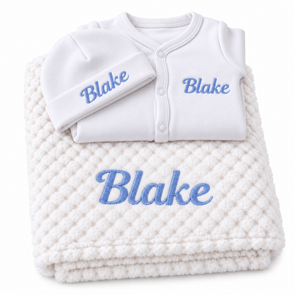 White set with blue embroidery showing personalised blanket, sleepsuit and hat on a white background.