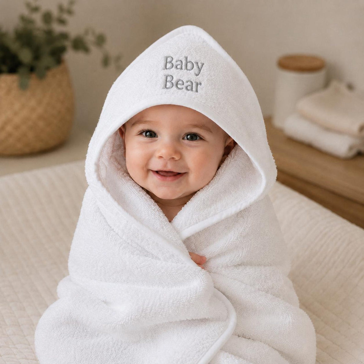 Baby wrapped in a white hooded towel with grey Baby Bear embroidery.