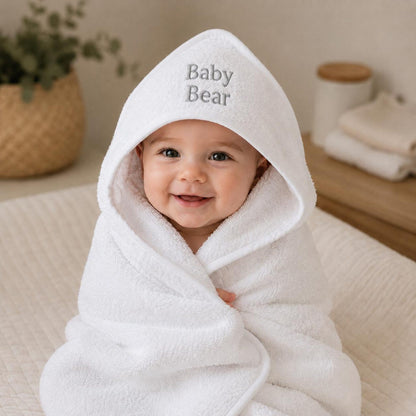 Baby wrapped in a white hooded towel with grey Baby Bear embroidery.